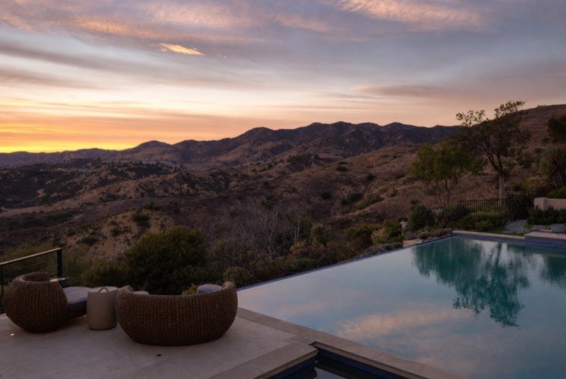 A hillside pool terrace overlooking green and gold canyon hills at dusk, like many homes around Calabasas