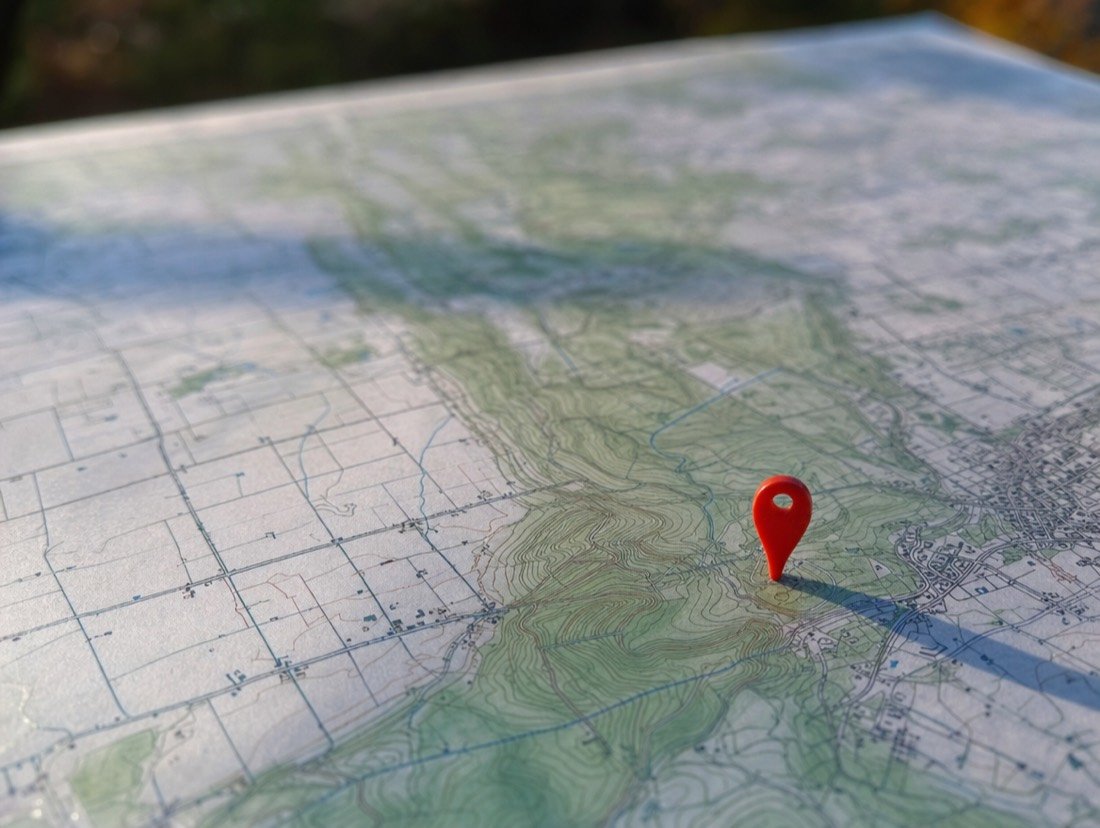 Close view of a scarlet map pin stuck into contour lines on a paper map