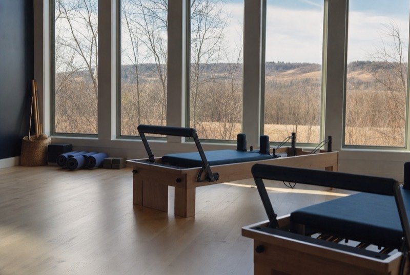 Reformer machines lined up on a light wood floor, rolled mats nearby, early sun coming in